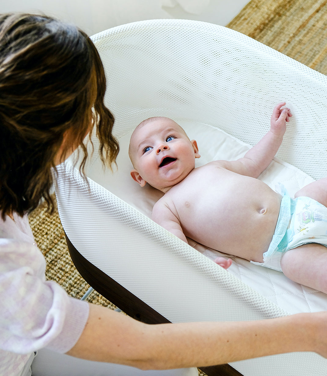 Baby laying on silkzees bassinet solution sheet inside of the Snoo by happiest baby while looking up at mom happily